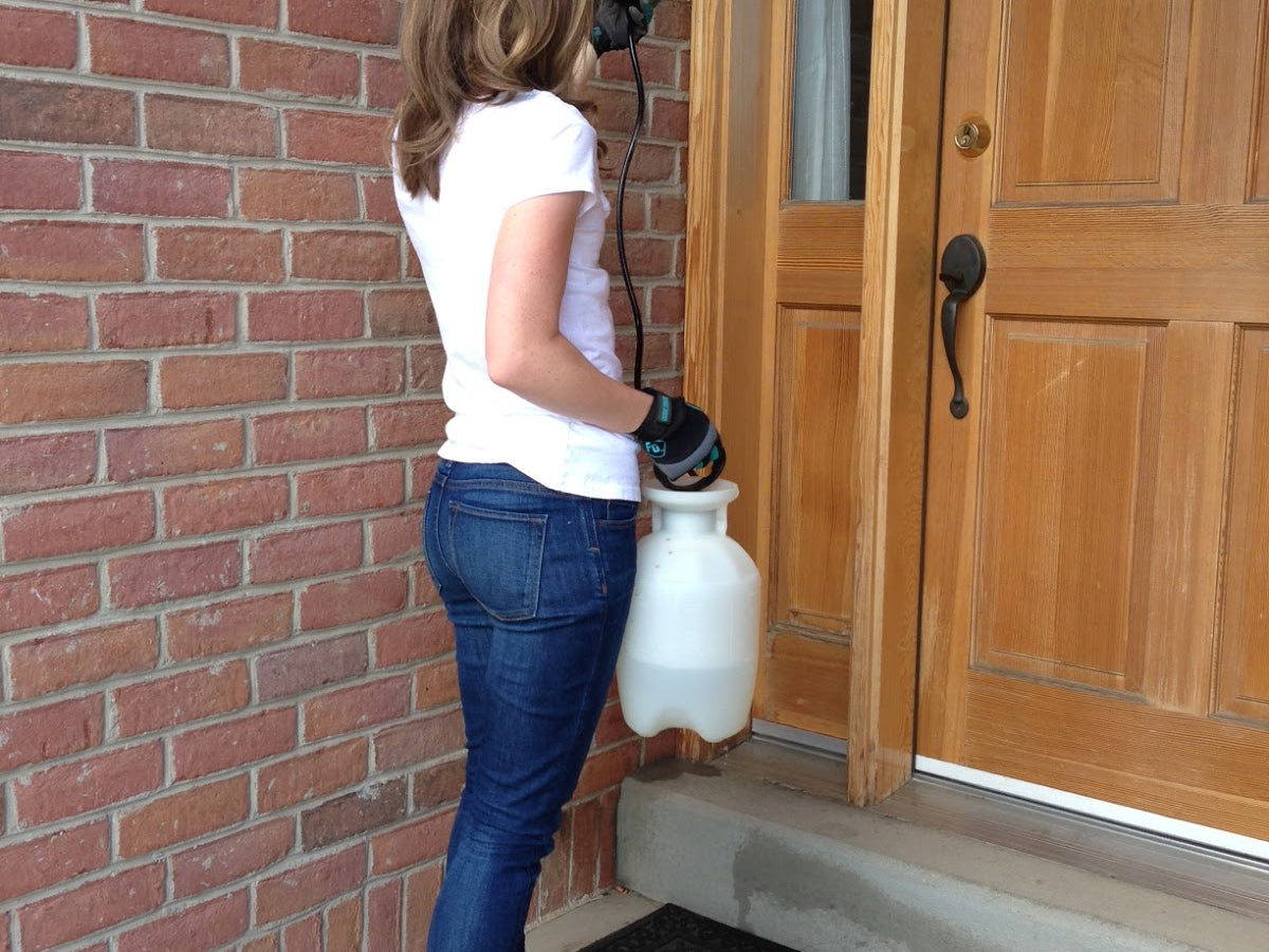 Person wearing white protective gear while holding pesticide solution in a white spray bottle
