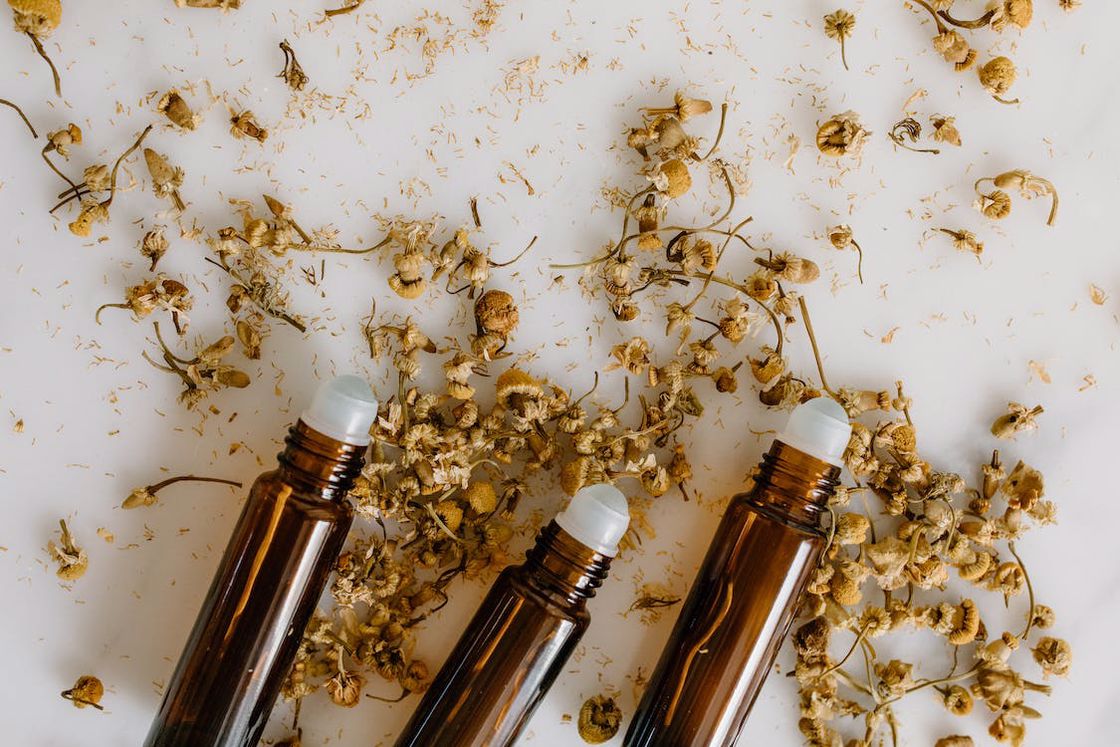 Three bottles of oil with rollers and dried flowers on a white table