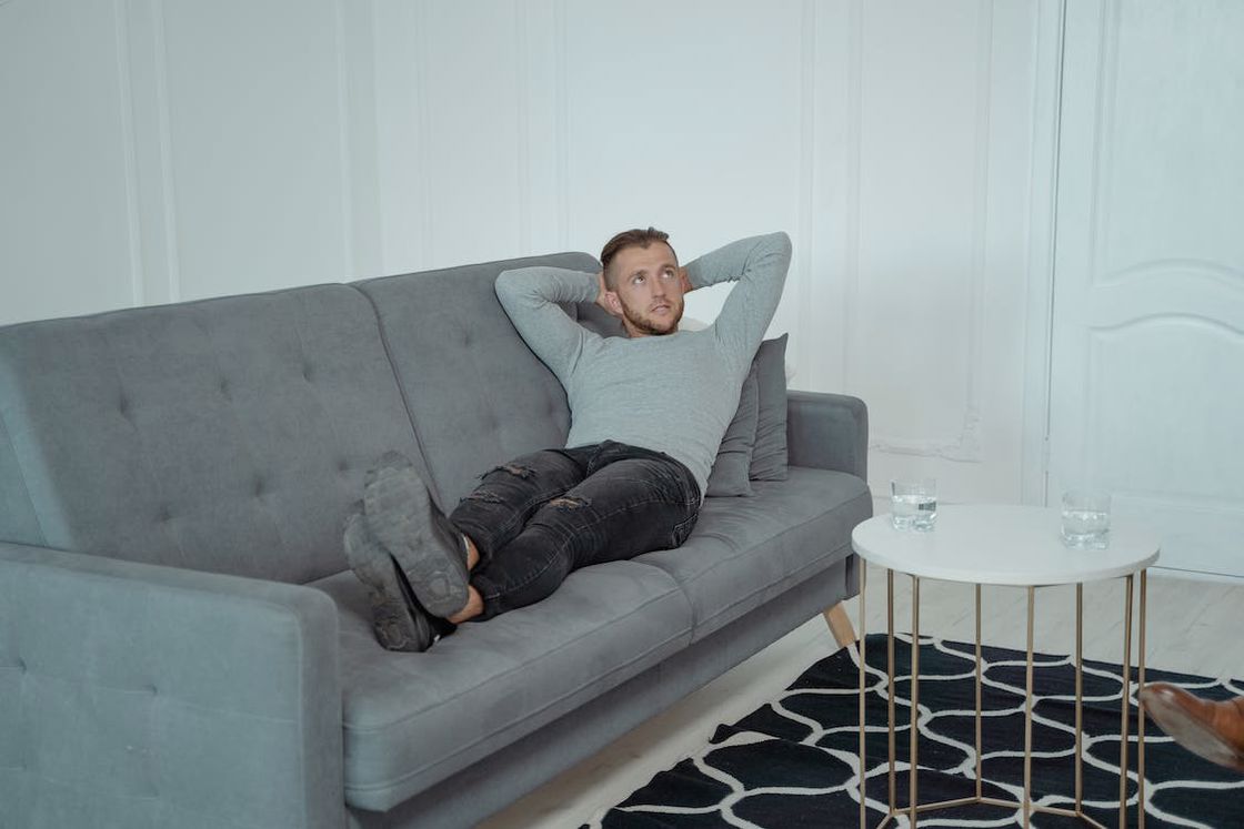 Man stretching his whole body on a gray couch