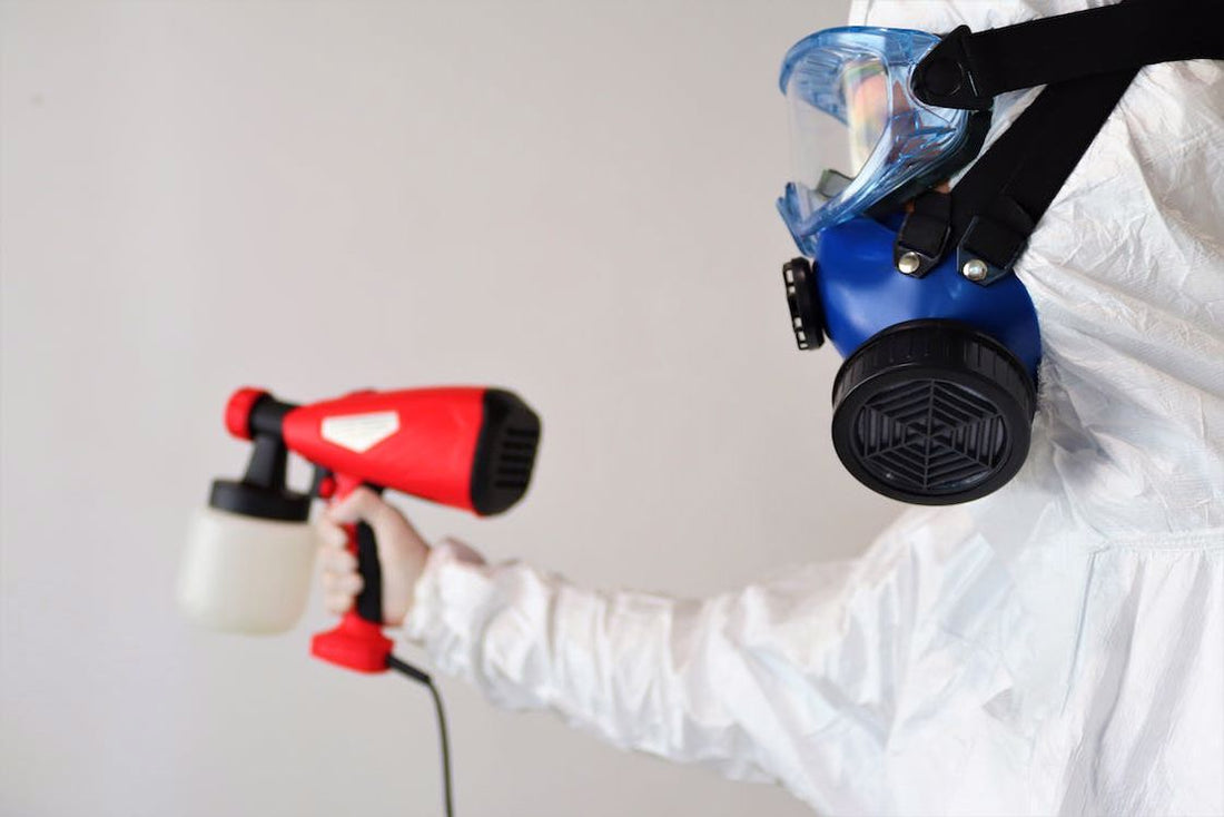 Person wearing white protective gear while holding a pest spray