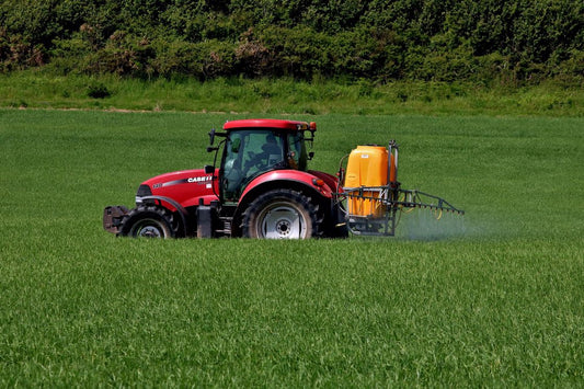 Red tractor spraying insecticide in a grass field