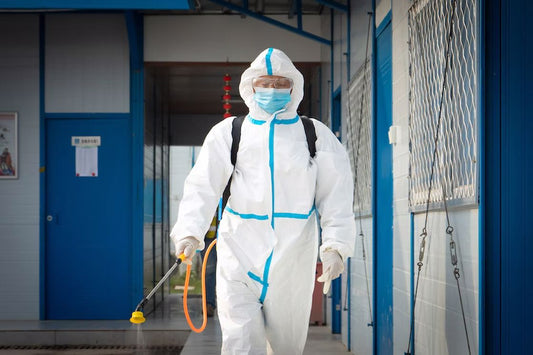 Man wearing white protective gear preparing to spray pesticide on a hallway